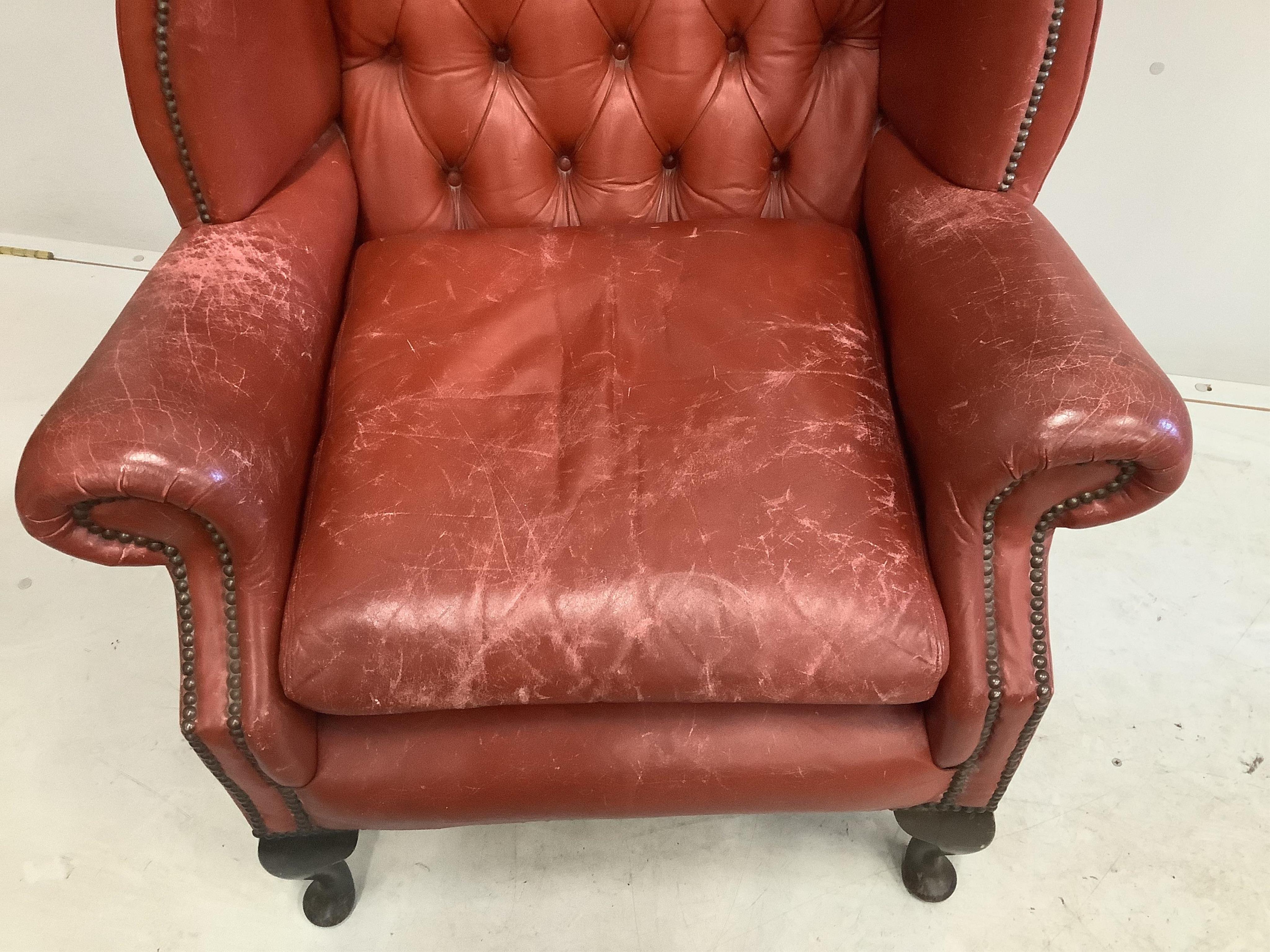 A Georgian style wing armchair with brick red leather upholstery, width 86cm, height 112cm. Condition - fair, but wear to the tops of the arms and seat